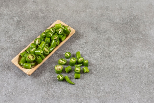 Wooden plate of sliced chili peppers on stone table. 