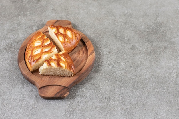 Wooden plate of sliced tasty pie on marble surface. 