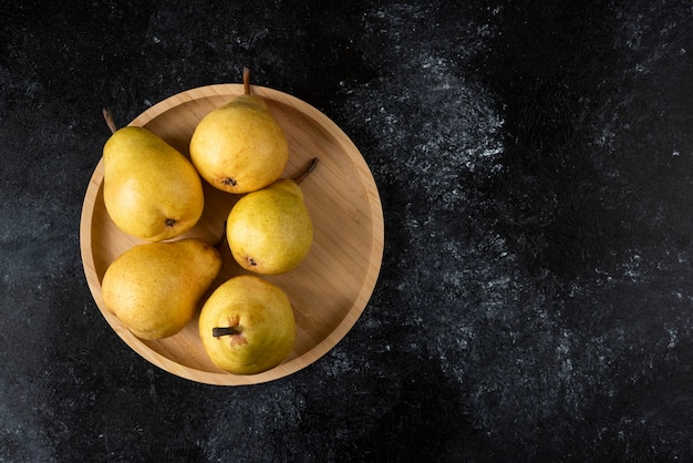 Free photo wooden plate of tasty yellow pears on black surface.