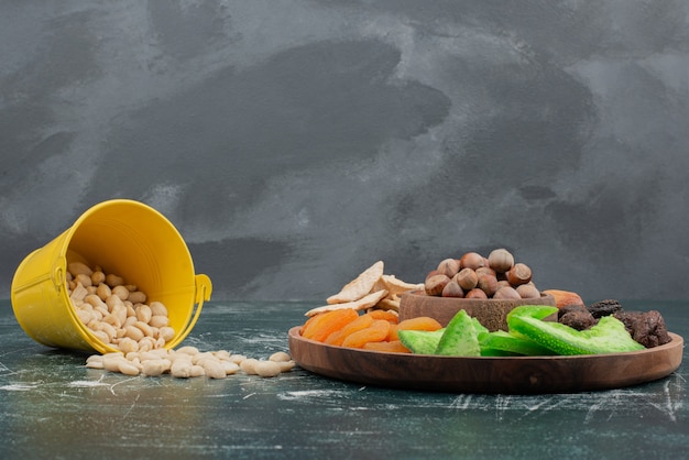 Free photo wooden plate with dried fruits and bucket of nuts .