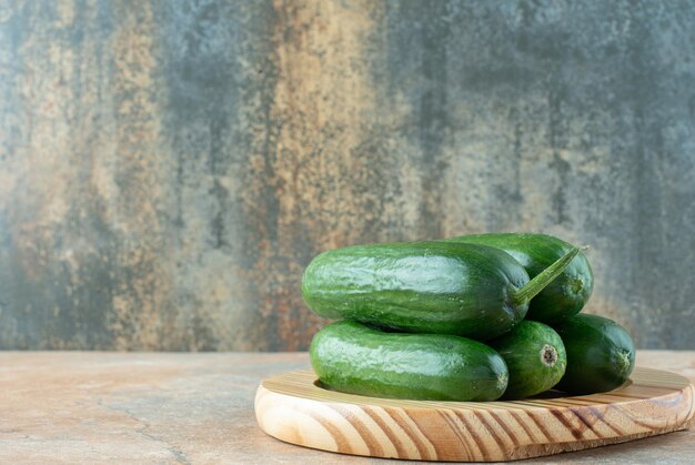 A wooden plate with fresh cucumbers on marble table.