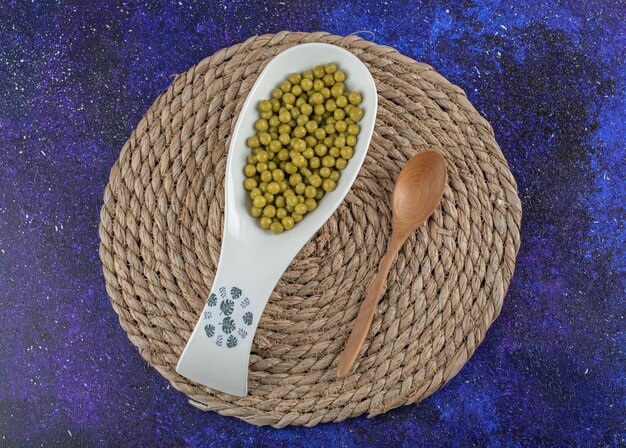 Wooden spoon and ceramic bowl full with marinated peas.