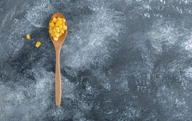 A wooden spoon full of popcorn seeds on marble.