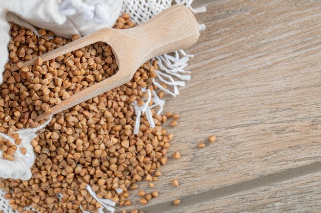 A wooden spoon full of raw buckwheat on a wooden table.