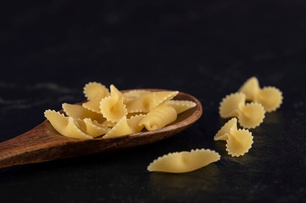 A wooden spoon full of raw farfalle tonde macaroni . 