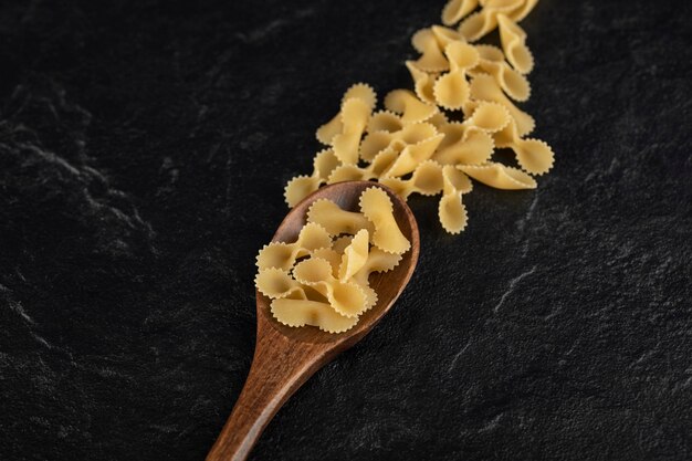 A wooden spoon full of raw farfalle tonde pasta. 