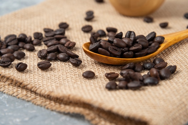 Wooden spoon full of roasted coffee beans on burlap.