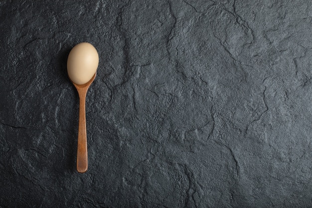 Wooden spoon of organic raw egg on black background