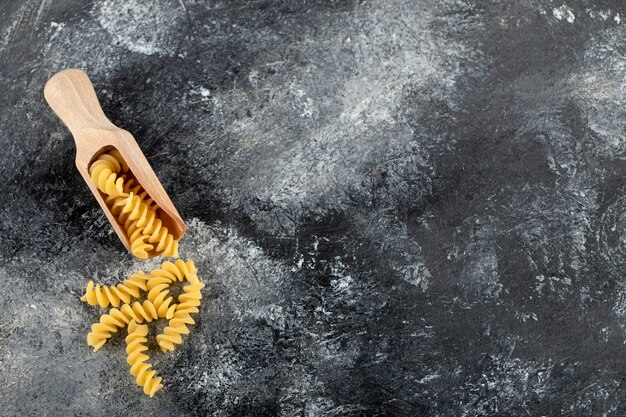 Wooden spoon of raw fusilli on marble surface