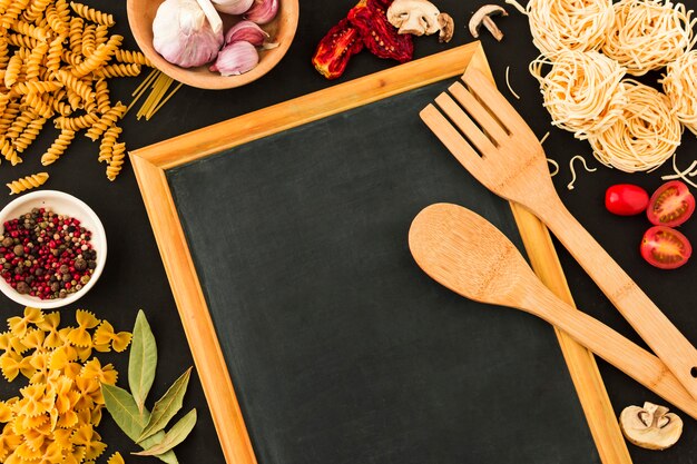 Wooden spoon and spatula on slate surrounded with pasta ingredients