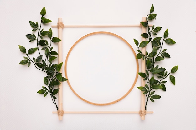 Wooden square and circle frame decorated with green leaves on white backdrop