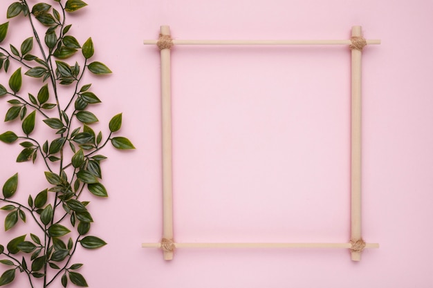 Free photo wooden square frame with artificial green leaves on pink backdrop