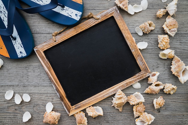 Wooden surface with blank slate, seashells and flip flops