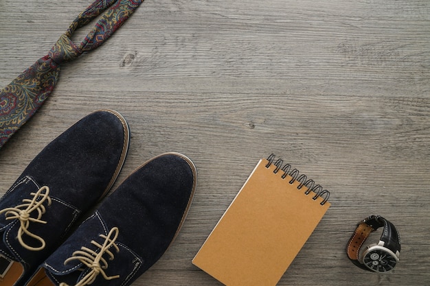 Wooden surface with necktie, shoes, watch and notebook