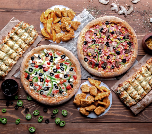 wooden table with pizzas and snacks on it