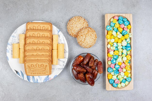 Wooden tray of popcorn candy, a small portion of dates, two cookies and biscuits lined up on a plate on marble background. High quality photo