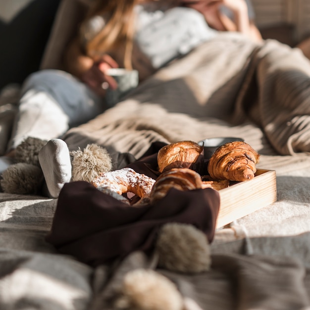 Free Photo wooden tray with baked croissant in front of couple lying on bed