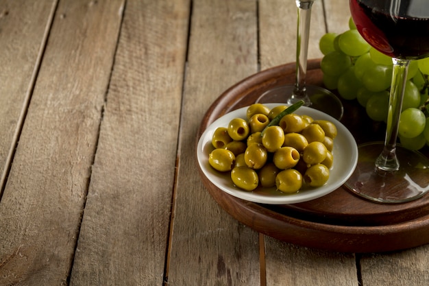 Free Photo wooden tray with olives, grapes and wine glasses