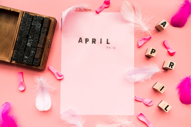 Free Photo wooden typographic blocks; balloons; feather; april blocks and april stamp on white paper against pink backdrop