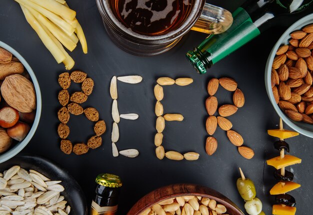 A word beer made from salted crispy nuts sunflower seeds and bread crackers salty snacks with string cheese bottles of beer and a mug of beer on black top view