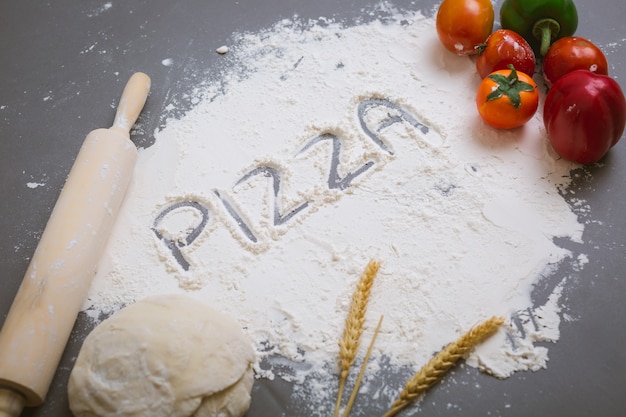 Free photo word pizza written on flour with ingredients