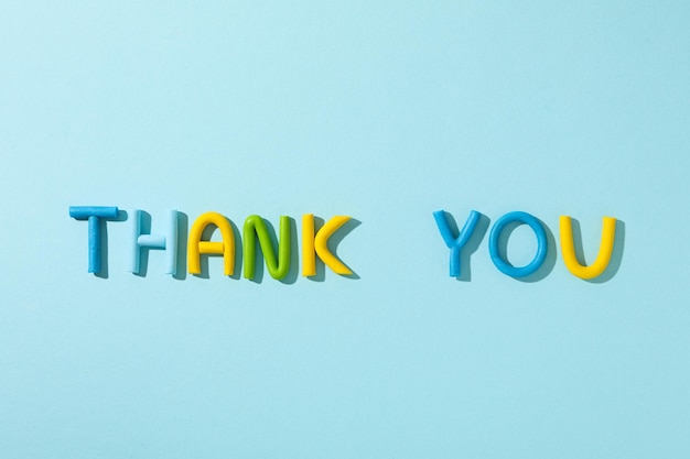 Free photo the word thank you from colored plasticine on a blue background