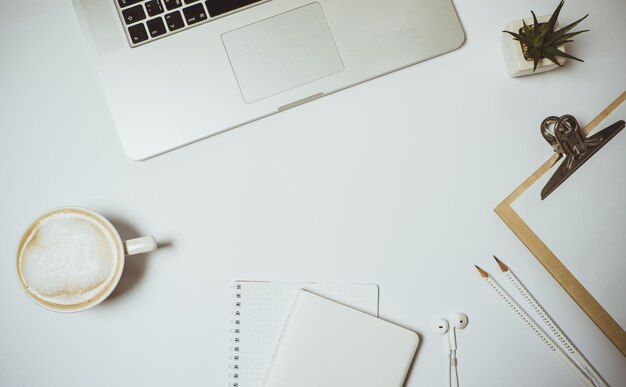 Work space with laptop coffee and stationery on white table Top view Flat lay