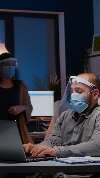 Free photo workaholic businessman with face mask and visor against covid working in company office