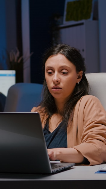 Workaholic entrepreneur woman sitting at desk table analysing financial graphics using laptop computer