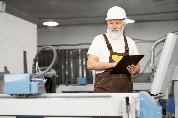 Worker of factory holding folder, observing laser cutter.