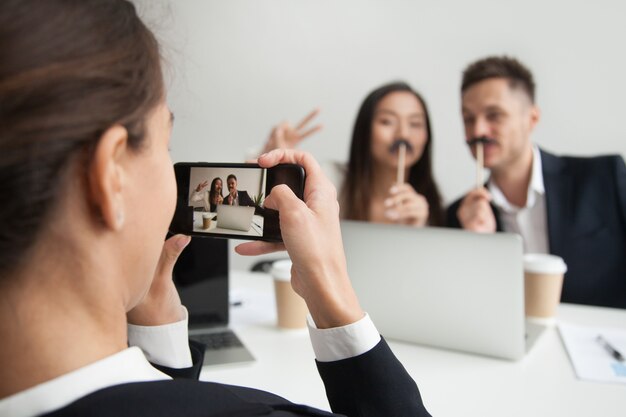 Worker making picture of colleagues trying mustache accessory