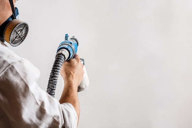 Worker painting wall with spray gun in white color.