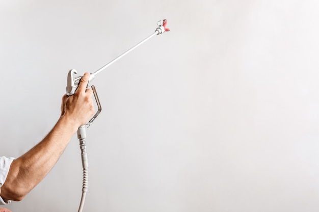 Worker painting wall with spray gun in white color.