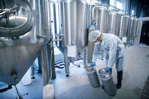 Free photo worker in protective suit carrying chemicals in metal reservoirs