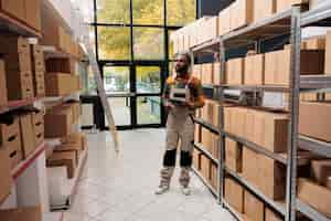 Free photo worker standing near racks filled with goods in carton boxes