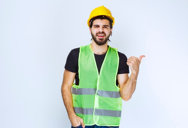 Worker in yellow helmet and gear pointing behind.