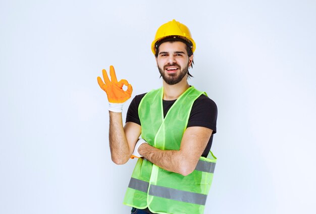 Worker in yellow helmet and workshop gloves showing enjoyment sign.