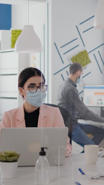 Workers wearing protective face mask talking about business project typing on pc in office during coronavirus global pandemic