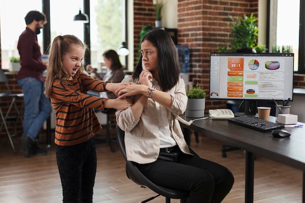 Working businesswoman irritated by annoying little girl while talking on telephone in agency office. Daughter disturbing busy mother talking on phone while in financial office workspace.