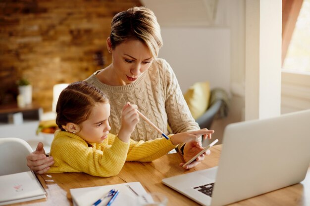 Working mother and daughter using mobile phone at home