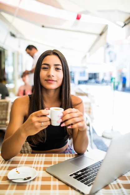 Working outdoors. Beautiful young woman in funky hat working on laptop and smiling while sitting outdoors