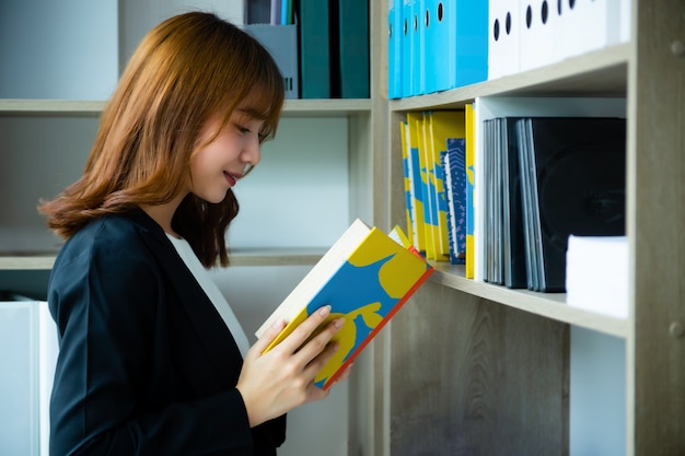 Working woman reading a book from shelves in library