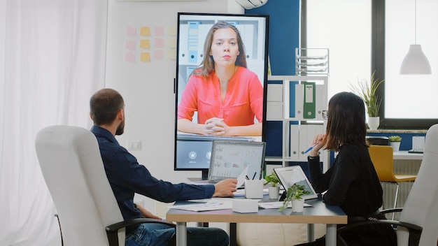 Free Photo workmates using video call on television for conversation with woman about business project. colleagues talking to manager on online conference for briefing strategy about presentation