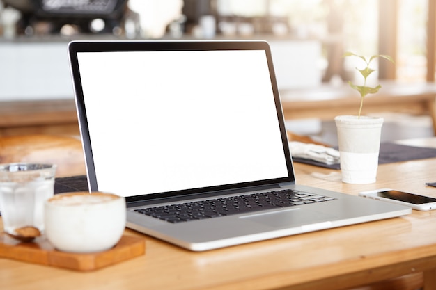 Free Photo workplace of self-employed person: generic laptop pc resting on wooden table with smart phone, mug of coffee and glass of water.