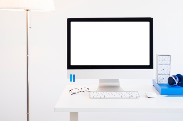 Workplace with keyboard near monitor, eyeglasses and headphones near lamp