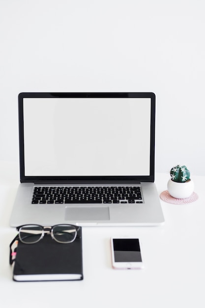 Workplace with laptop near eyeglasses, notebook and smartphone