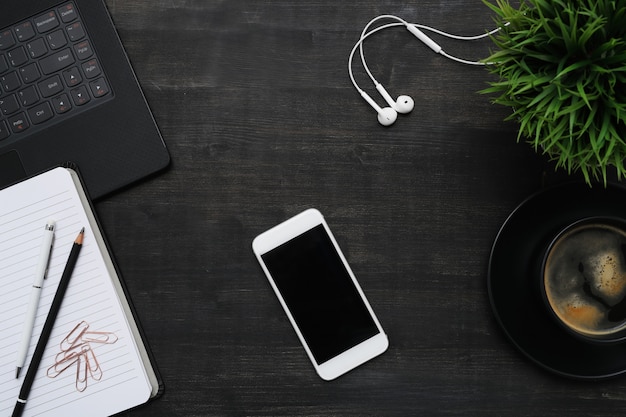 Workplace with smartphone, coffee cup, notebook, on black table. Top view