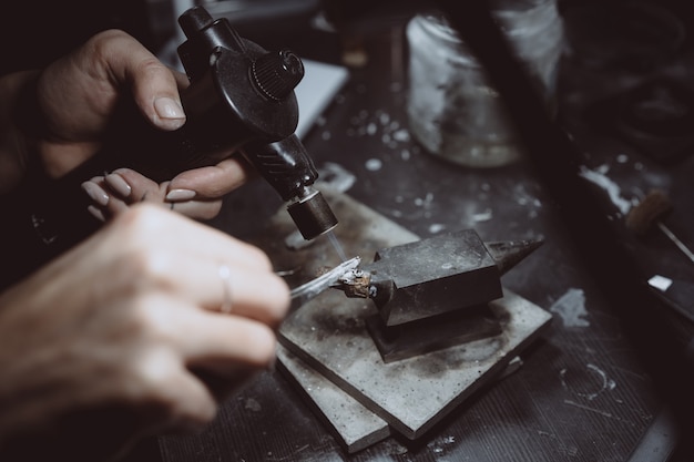 In the workshop, a woman jeweler is busy soldering jewelry