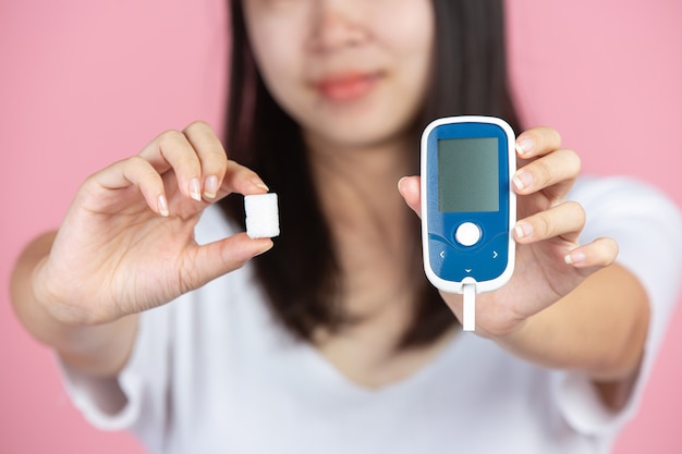 Free photo world diabetes day; woman holding glucose meter and sugar cubes on pink wall