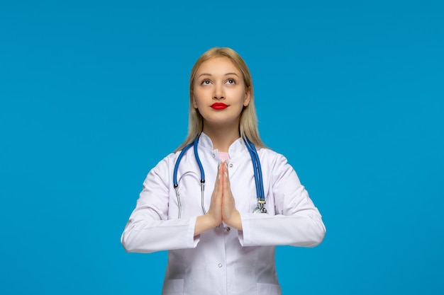 World doctors day praying blonde young doctor holding hands with the stethoscope in the lab coat